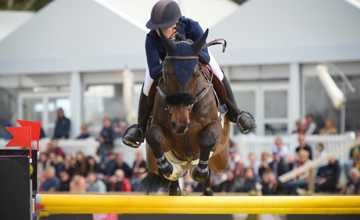 Horses jumping in arena with spectators