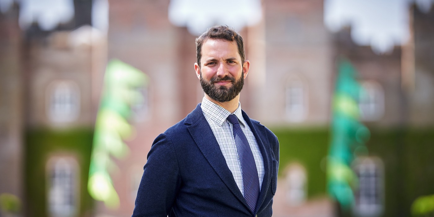 head and shoulder photo of William Stormont wearing a navy suit jacket and tie, with the front of scone palace blurred in the background.