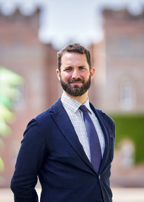 head and shoulder photo of William Stormont wearing a navy suit jacket and tie, with the front of scone palace blurred in the background.